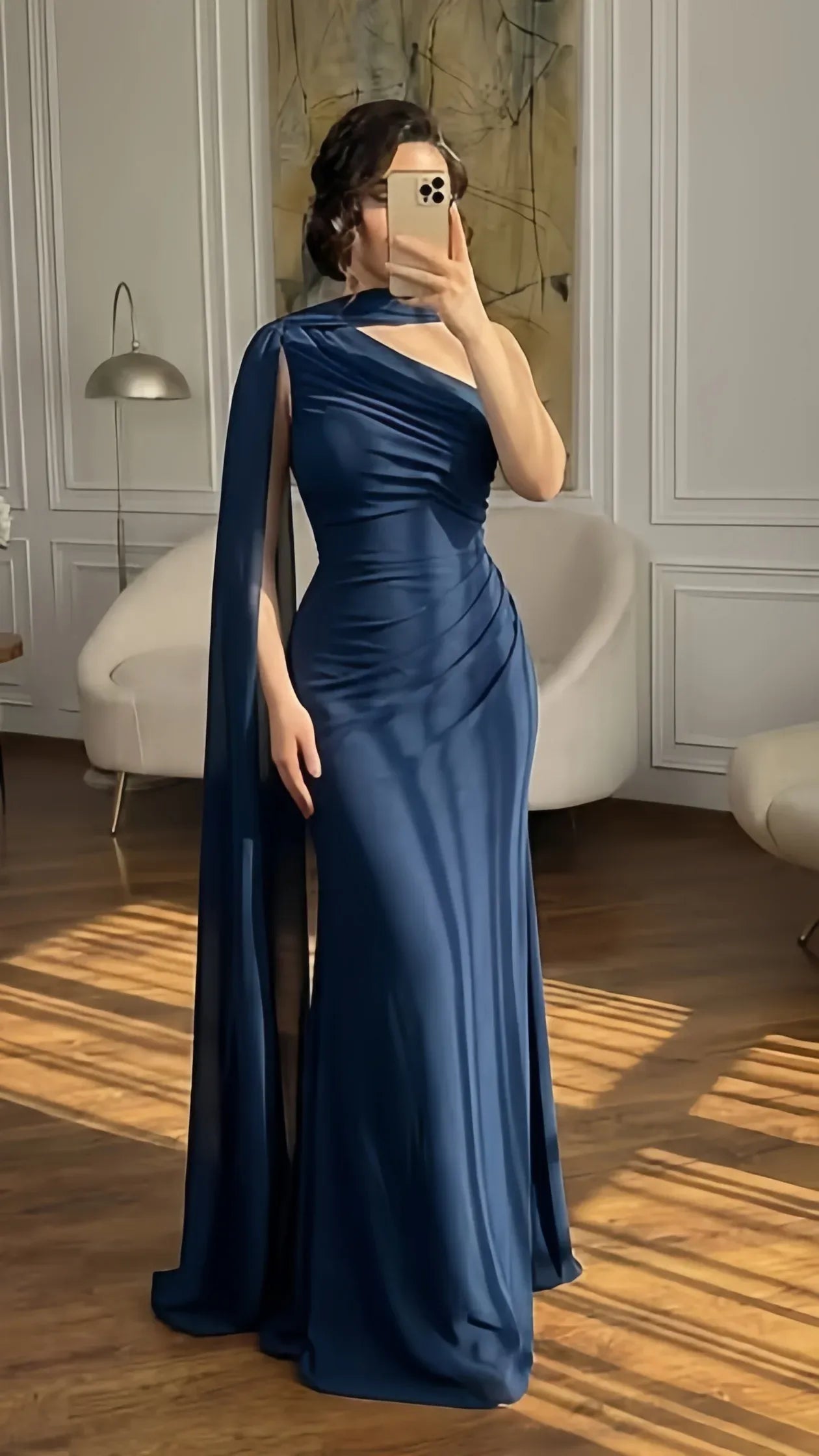 Elegant navy mermaid prom dress with one-shoulder cape sleeve and ruched side detail.