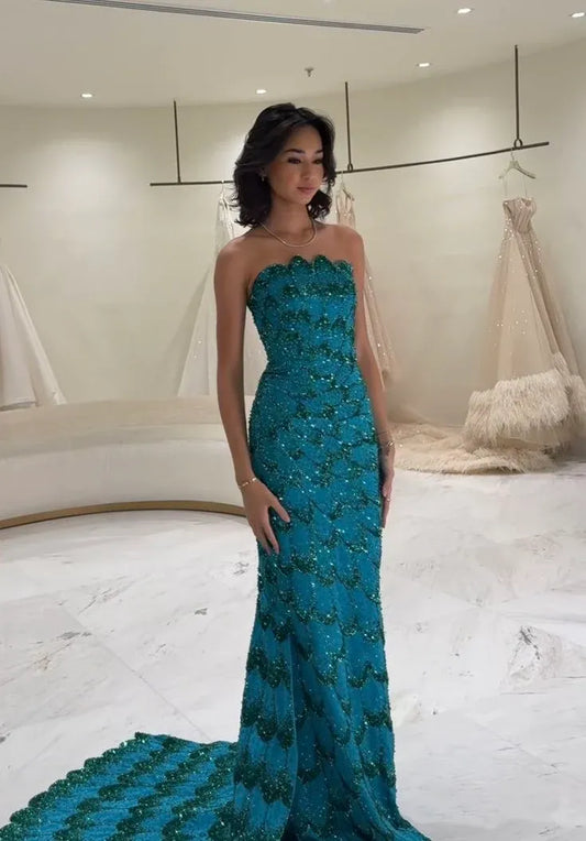 Model in a peacock-teal sequin mermaid prom gown, showcasing the strapless neckline and flowing train.