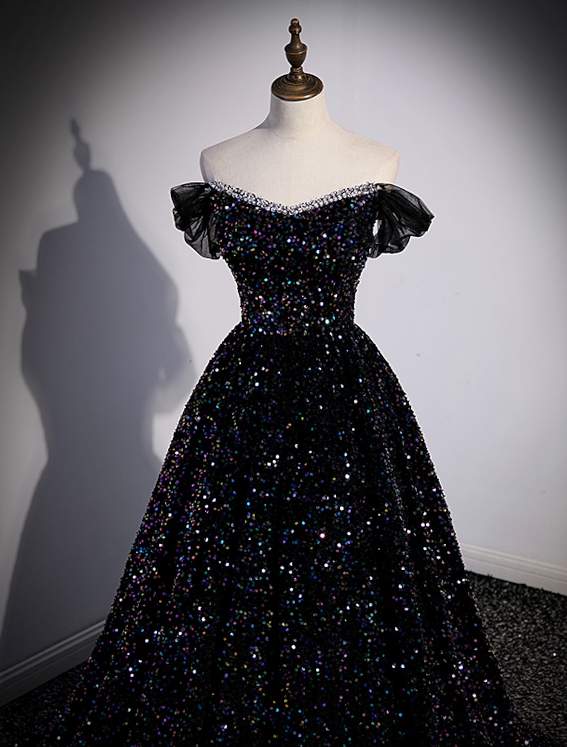 Side profile of a pleated sequined off-shoulder ball gown.